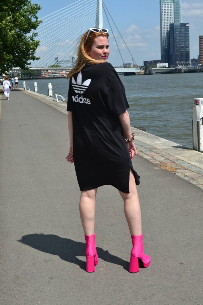 a girl is taking picture in adidas oversized black t-shirt with pink shoes 